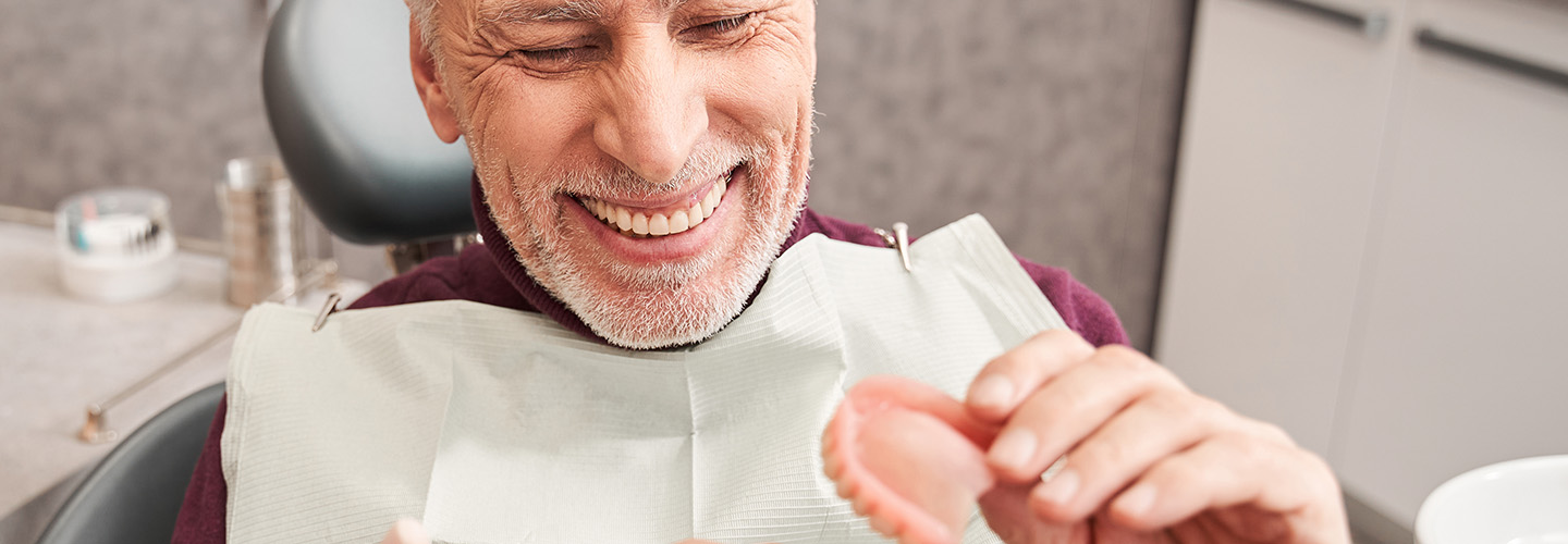 Dentist showing to senior patient teeth dentures