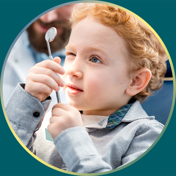 Child looks at himself in a dentist's mirrored tooth inspection tool.