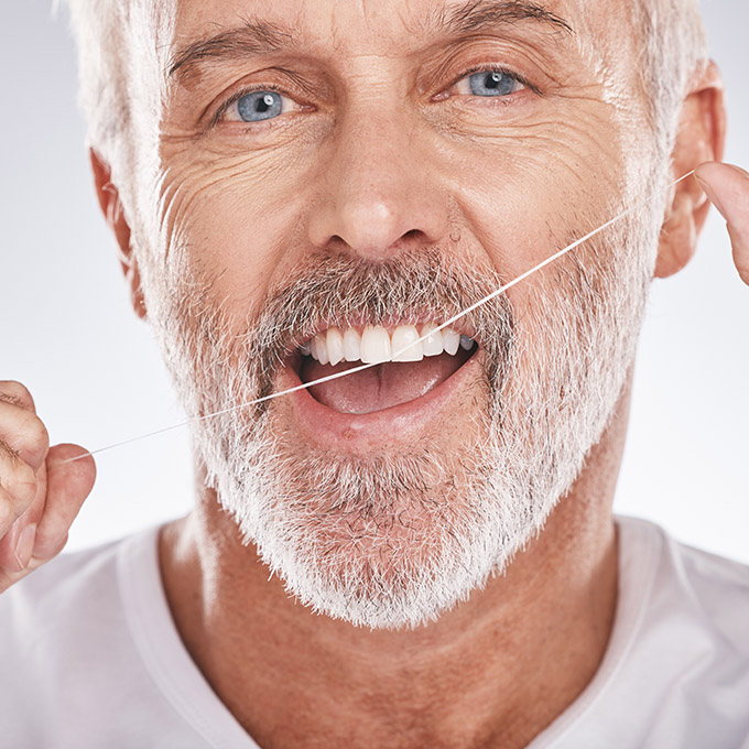 Dental, floss and face of senior man in studio isolated on a gray background. Portrait, cleaning or elderly male model with product flossing teeth for oral wellness, healthy gum hygiene or tooth care